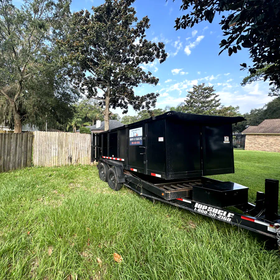 black dumpster hauling on a patio with grass and trees around